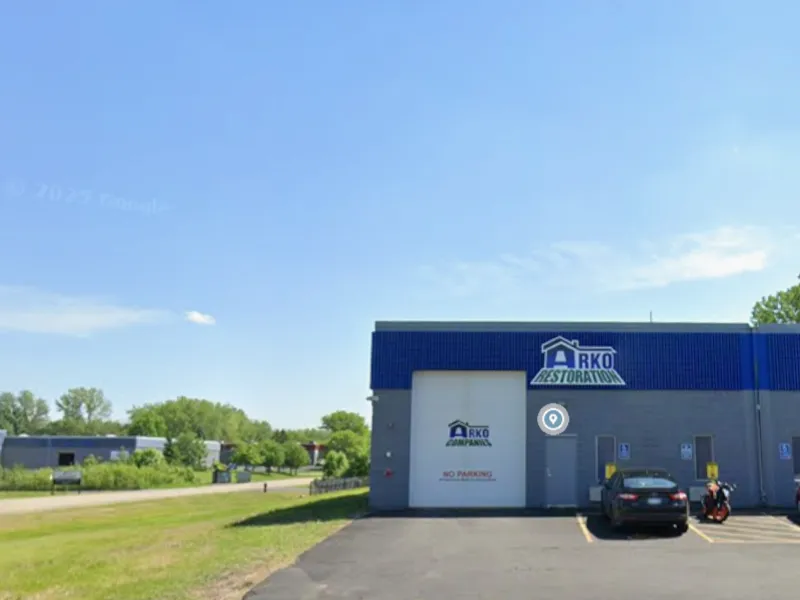 Commercial building with a blue roof labeled "ARKO Restoration" and a parking lot with cars.