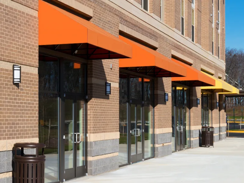 Row of glass doors with orange and yellow awnings on a brick building exterior.