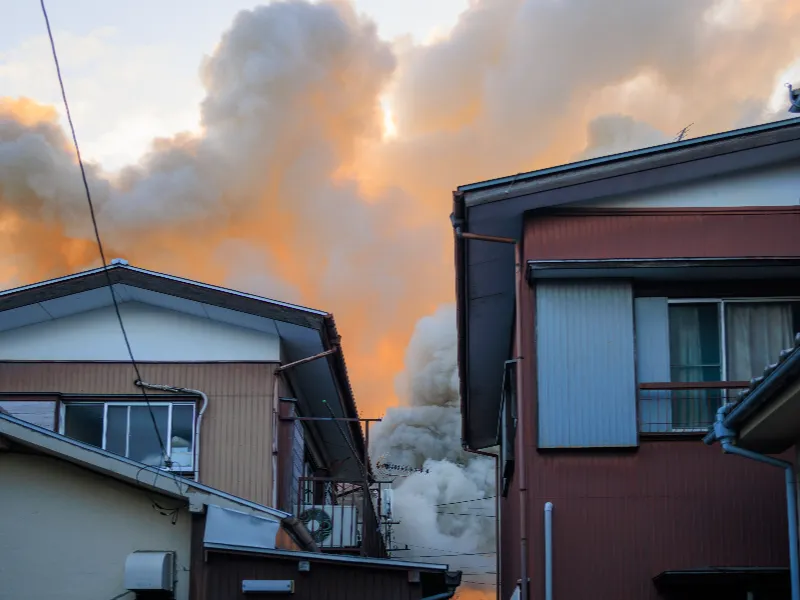 Thick smoke billows behind residential buildings at sunset.